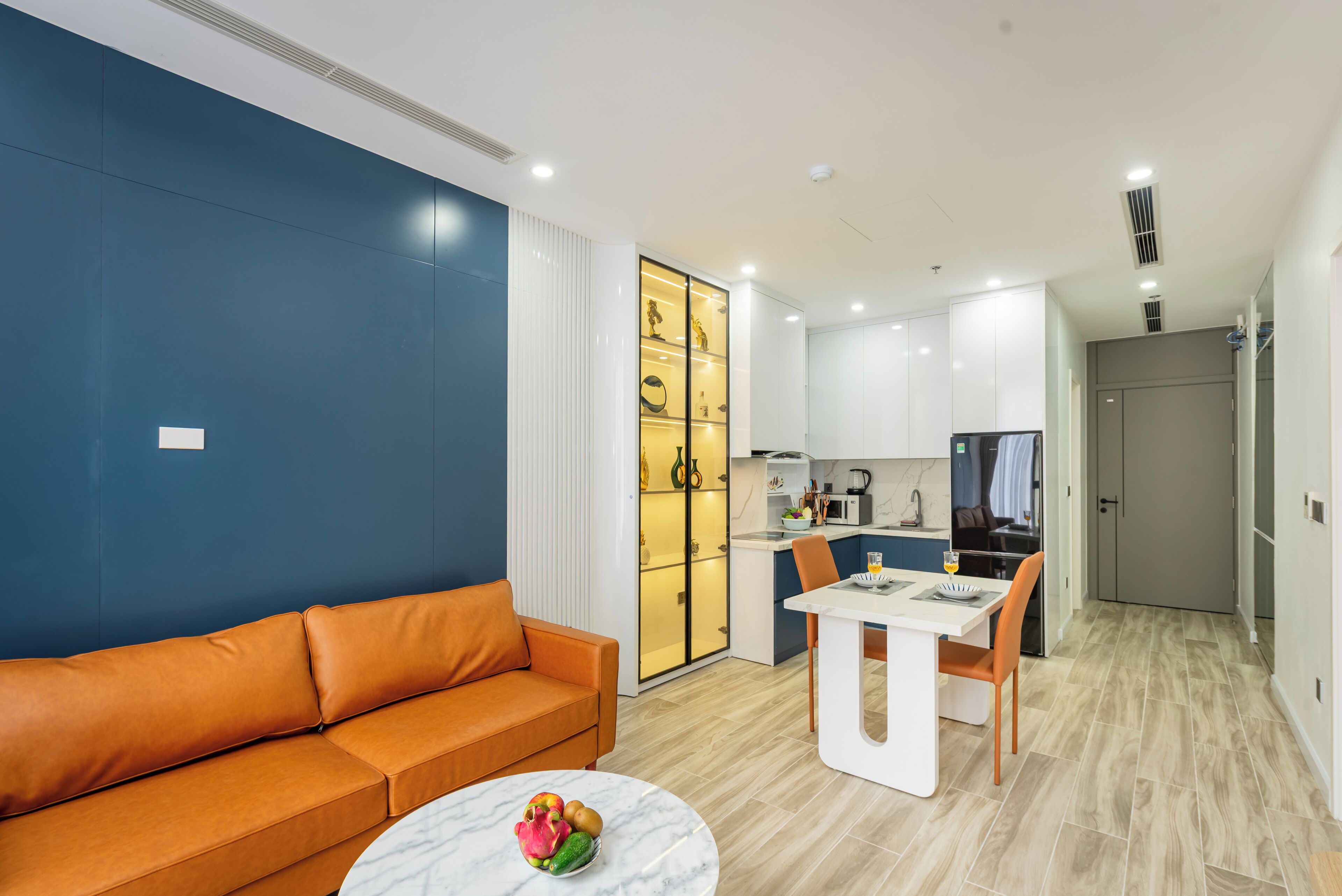 A modern living room with a sofa, a dining table with chairs, and a kitchen area with cabinets and appliances.
