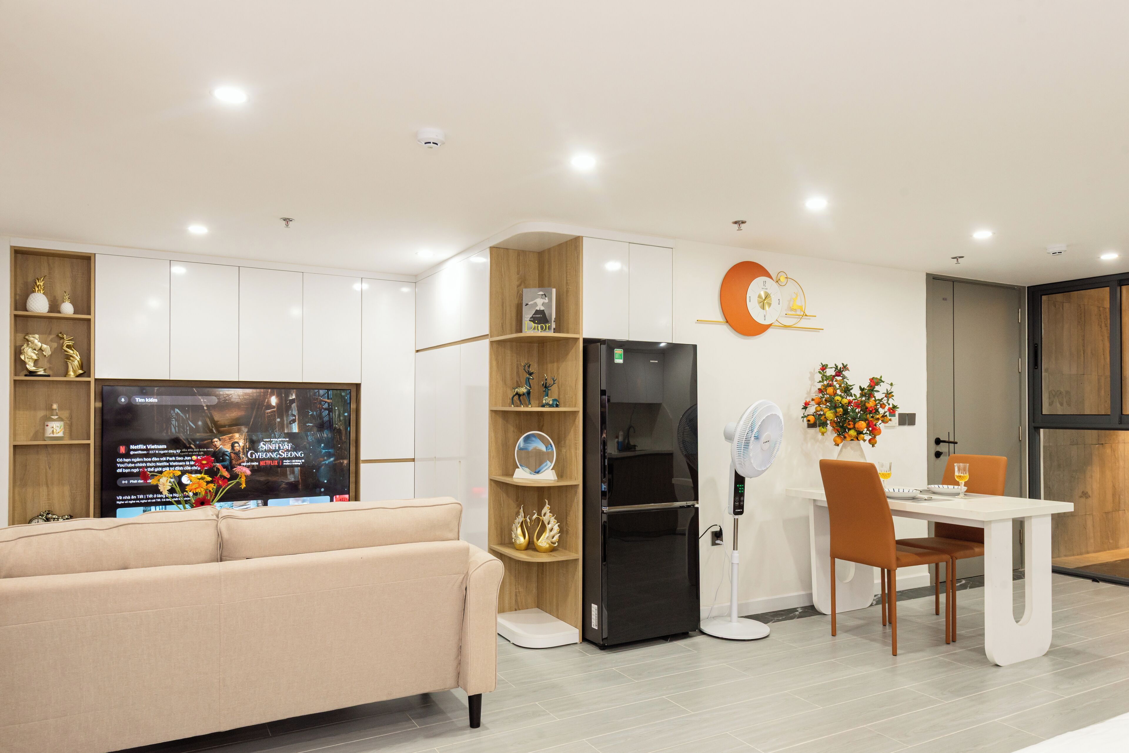 A modern kitchen with a built-in refrigerator, a dining area with a white table and chairs, and a beige sofa.