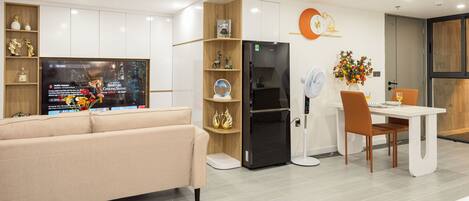 A modern kitchen with a built-in refrigerator, a dining area with a white table and chairs, and a beige sofa.