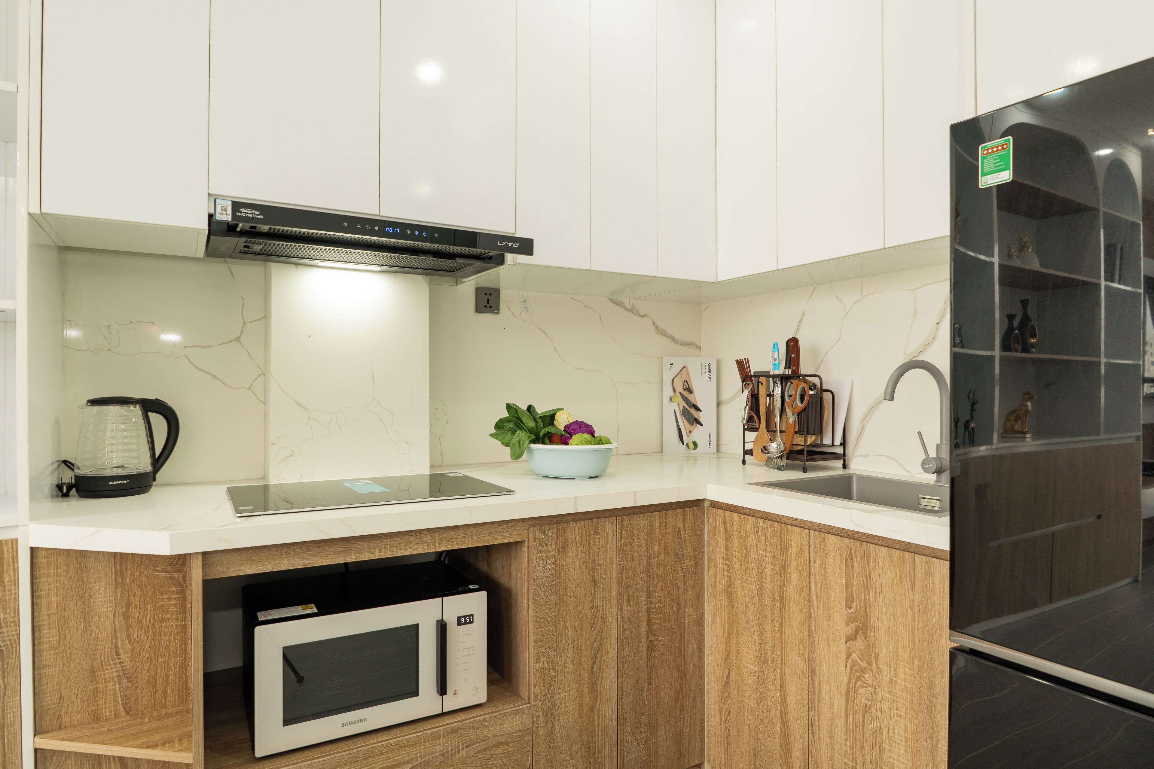 Una cocina moderna con muebles blancos, microondas integrado, refrigerador de acero inoxidable y una campana extractora negra.