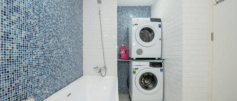 Ein Badezimmer mit einer weißen Badewanne, zwei übereinander gestapelten Waschmaschinen und blauen Mosaikfliesen an den Wänden.