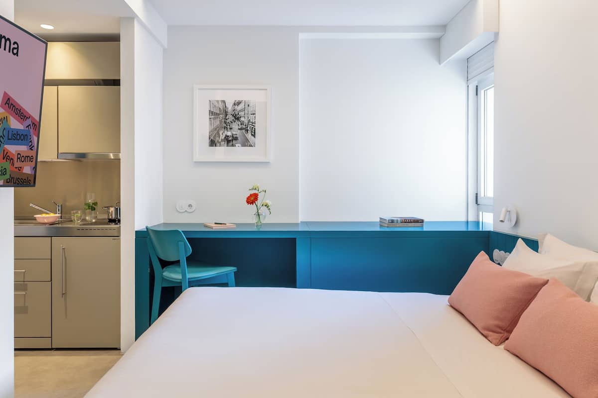 Une chambre d’hôtel moderne équipée d’un lit, d’un bureau, d’une chaise, d’une fenêtre et d’un coin cuisine.