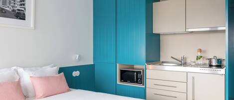 Una habitación de hotel moderna con cama, kitchenette y un cuadro en la pared.