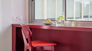 A modern dining area with a red chair and table, a bowl of lemons, a glass of water, and a pitcher of mint-infused water on the windowsill.