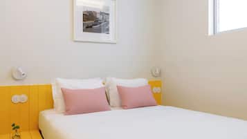 A neatly arranged hotel room with a bed, pillows, a bedside table with a book, and a wall-mounted picture.