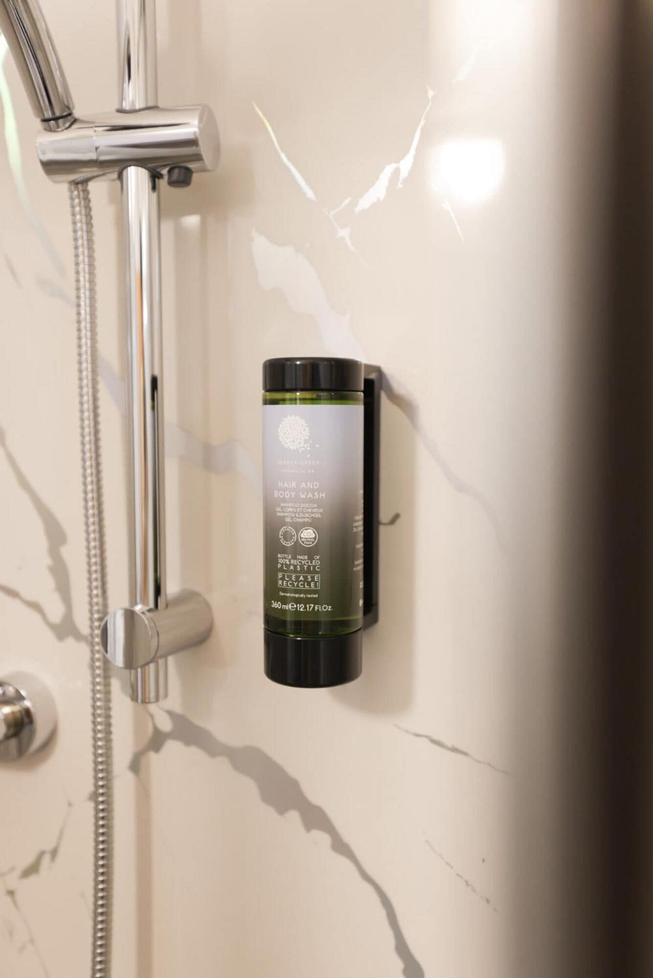 Casa de banho com chuveiro, um frasco de gel de cabelo e corpo, e um secador de mãos.
