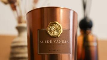 A copper-colored candle labeled "SUEDE VANILLA" with a gold emblem, placed on a wooden surface.
