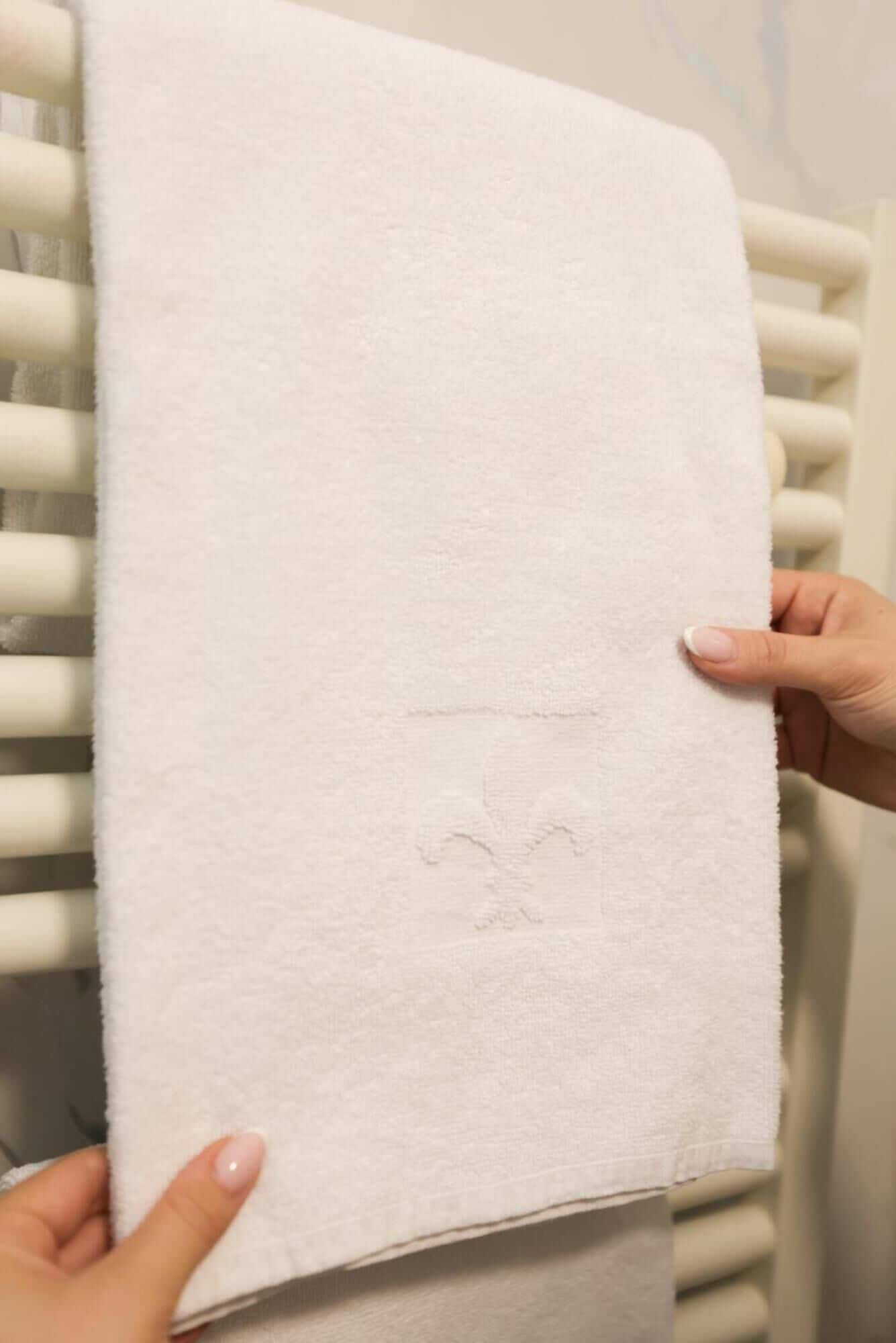 Una toalla blanca con un logotipo, sostenida por una persona con uñas cuidadas.