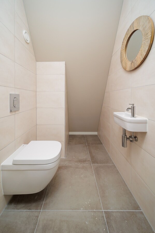 A small, modern bathroom with a toilet, sink, and a mirror on the wall.