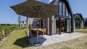Une maison moderne dotée d’un patio, d’une table à manger et d’un parasol.