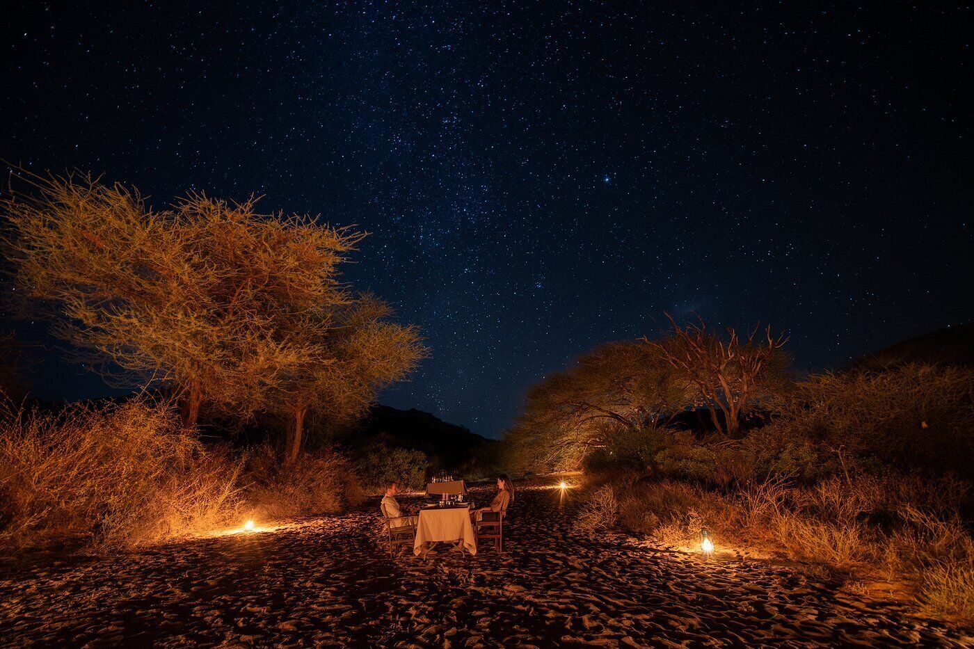 A night scene with a starry sky, a table with chairs, and a person sitting.