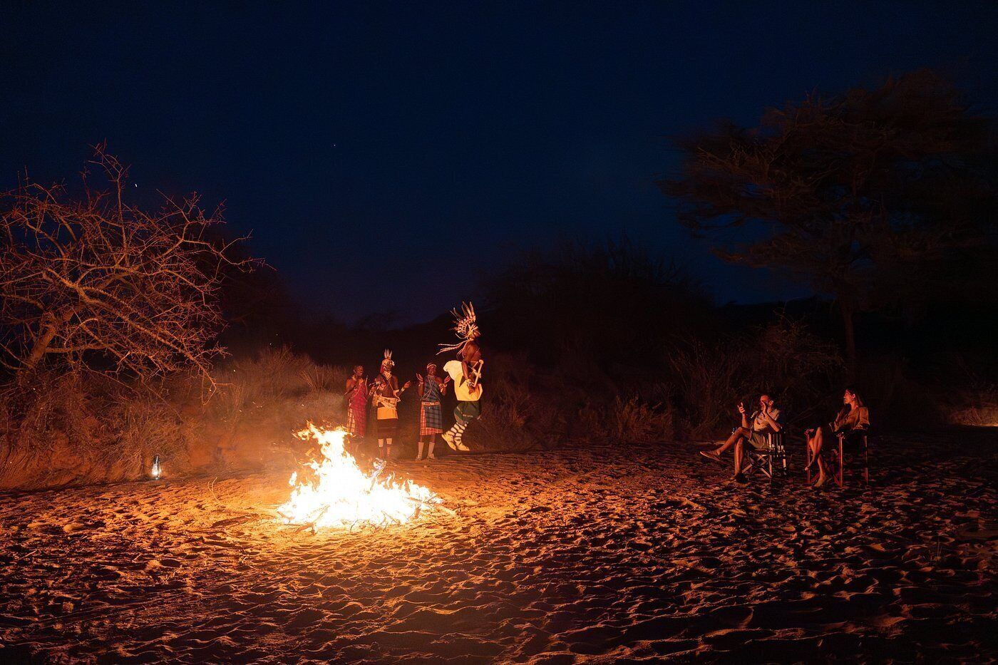 A group of people around a campfire in a natural setting at night.