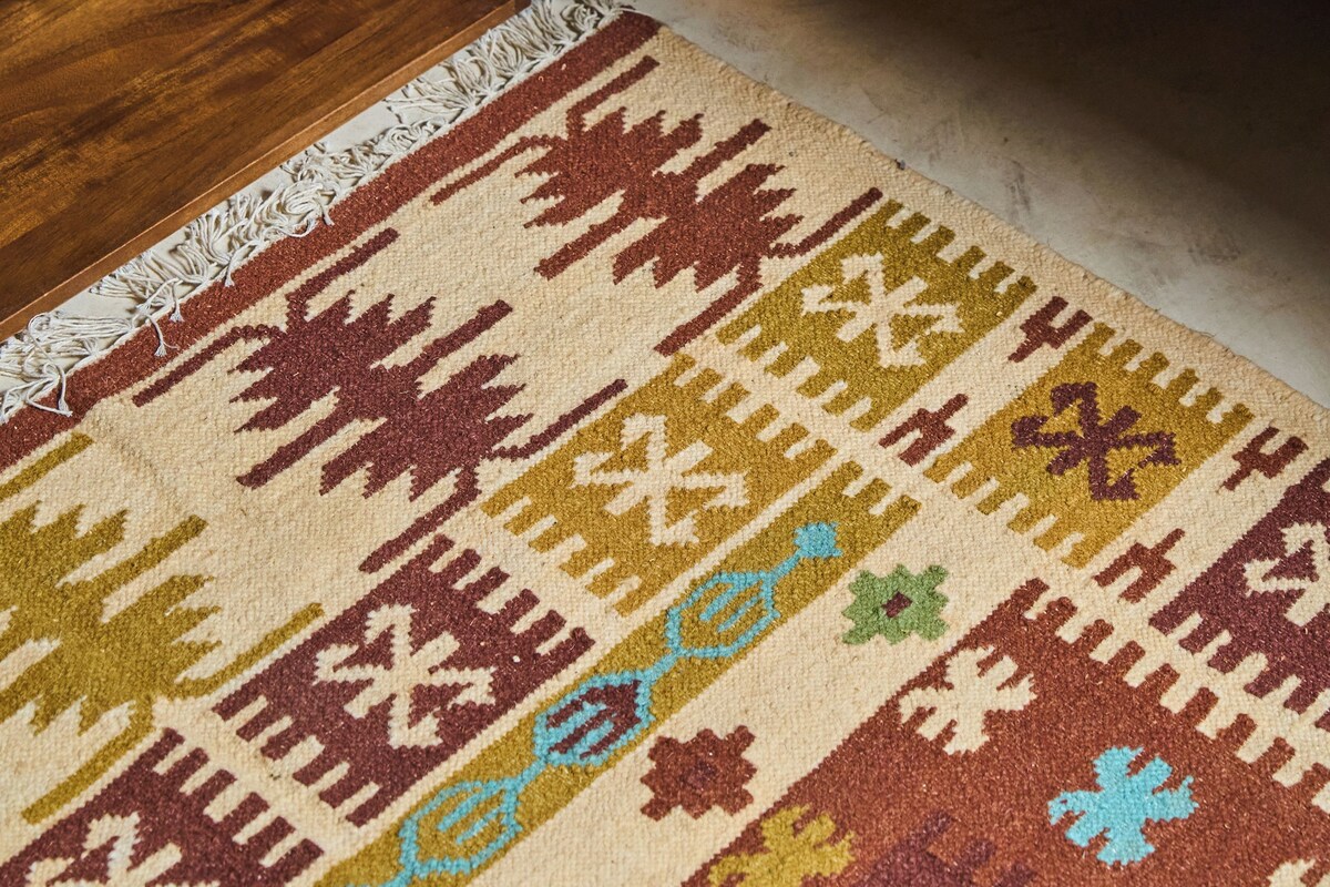 A wooden bedside table, a patterned rug, and a bed with white bedding.