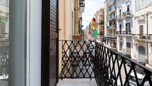 Un balcon doté d’une balustrade en fer forgé, donnant sur une rue bordée de voitures garées et d’immeubles.