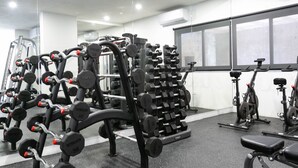 Een sportschool met diverse fitnessapparaten, waaronder gewichten, een bank en cardio-machines.