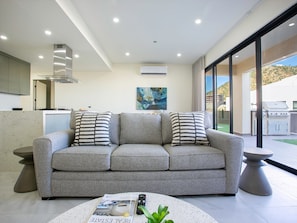 A modern living room with a grey sofa, two striped pillows, a remote control, and a magazine on a round coffee table. - Casa Lumar in Cabo San Lucas (Cabo San Lucas)