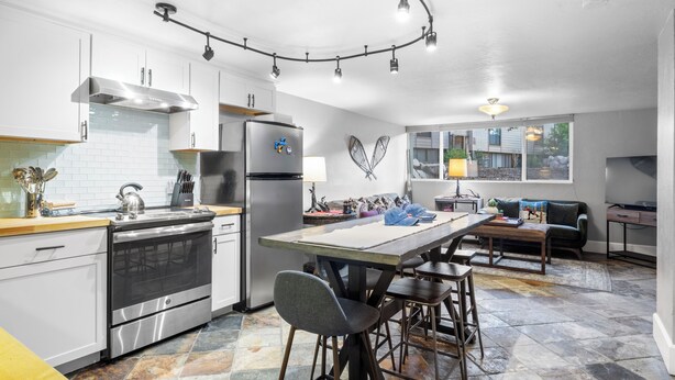 Una cocina moderna con una isla central, electrodomésticos de acero inoxidable y una zona de comedor con sofá y mesa.