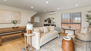 A modern living room with a sofa, coffee table, and ottoman, a wooden bench, and a large abstract painting on the wall. - Modern 5BDR, Mins to Sunset Cliffs & Ocean Beach | Point View Luxe by AvantStay (San Diego)