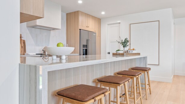 Una cocina moderna con encimera de mármol, electrodomésticos de acero inoxidable, taburetes de madera y una puerta blanca grande.