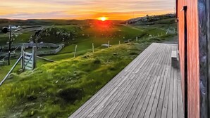 A wooden deck with a view of a sunset over a grassy landscape.