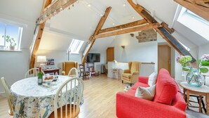 A cozy loft apartment with exposed wooden beams, a dining area with a floral tablecloth, a red sofa, and a bookshelf. - 2 bedroom accommodation in Durham (Durham)