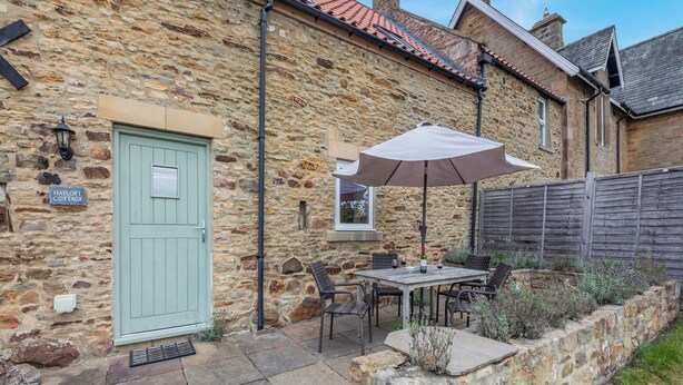 A stone cottage with a green door, a patio with a table and chairs, and an umbrella. - 2 bedroom accommodation in Durham (Durham)