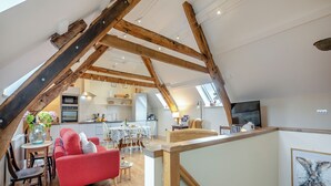 A spacious loft apartment with exposed wooden beams, a kitchen, dining area, and a living room with a red sofa and a glass coffee table. - 2 bedroom accommodation in Durham (Durham)
