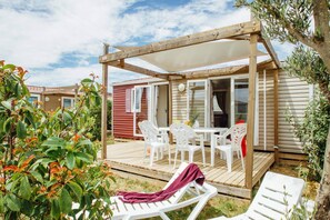 Une terrasse en bois avec une table et des chaises, un espace salon couvert et une vue sur un bâtiment voisin.