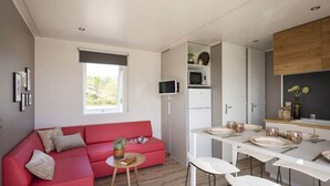 A compact living space with a red sofa, a small round table, a dining table set for four, and a kitchen area with a microwave and cabinets. - Mobile Home in Bessan With Terrace (Bessan)