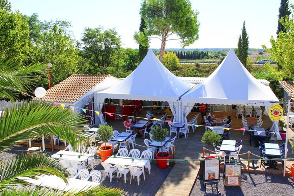 A rooftop terrace with white tables and chairs, surrounded by potted plants and a view of the countryside. - Mobile Home in Bessan With Terrace (Bessan)