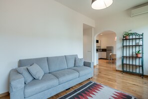 A living room with a grey sofa, a patterned rug, and a metal plant stand.