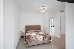 Een moderne slaapkamer met een bed, nachtkastjes, een deur en een plafondlamp.