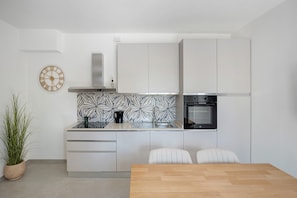 A modern kitchen with white cabinetry, a black oven, and a decorative clock.