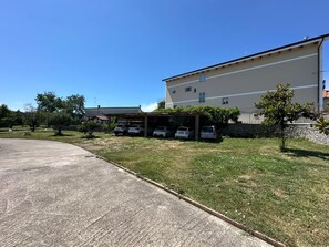 Een gebouw met een parkeerplaats, een overdekte parkeergarage en een grasveld met bomen.
