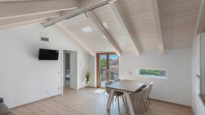 A modern interior with a dining area, a TV mounted on the wall, and a view through a glass door. - Suite Le Orchidee with Mountain View, Wi-Fi and Air Conditioning (Agerola)