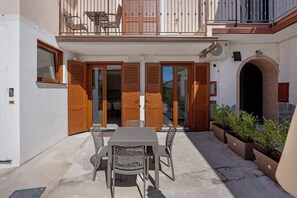 Un patio con una mesa, sillas, contraventanas de madera y un arco de ladrillo.