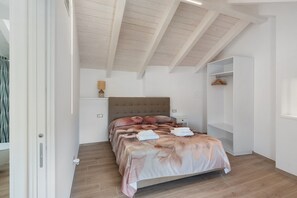 Quarto com cama, soalho de madeira, cabeceira, guarda-roupa e mesa de cabeceira.