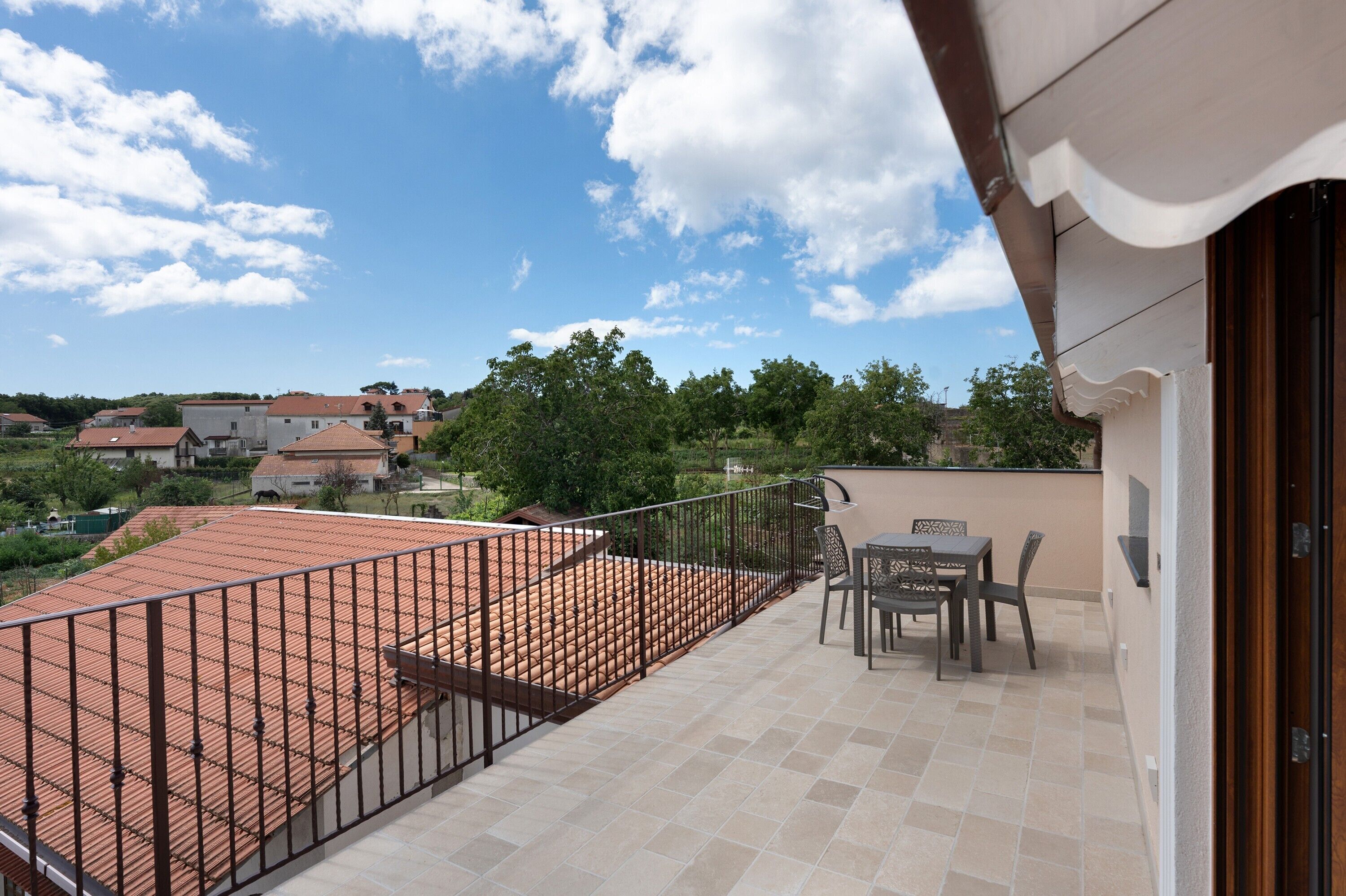 A balcony with a tiled floor, a metal railing, and a table with chairs.