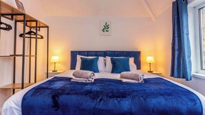A neatly made bed with a blue bedspread and pillows, two bedside lamps, and a wall-mounted plant. - Bright & Spacious 3 BR House in Haltwhistle (Haltwhistle)