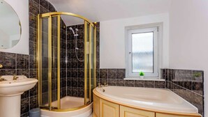 A bathroom with a curved shower enclosure, a freestanding bathtub, a sink, and a window with a view of the outside. - Bright & Spacious 3 BR House in Haltwhistle (Haltwhistle)