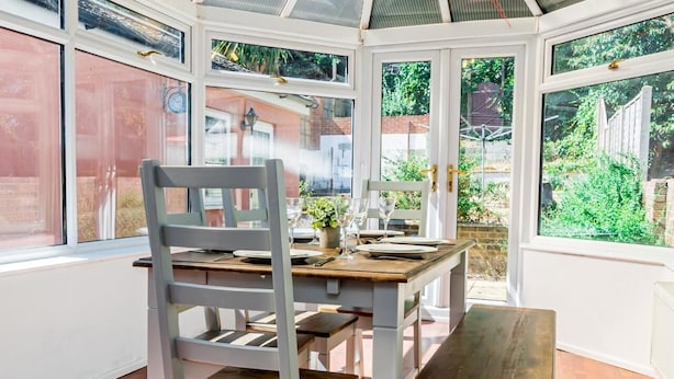 A conservatory with a dining table and chairs, large windows, and a view of the garden.