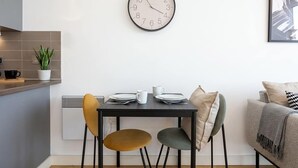 A modern kitchen with a round wall clock, a dining table with chairs, and a sofa in a living area. - Stunning Skyline 1BR Liverpool Apartment w Parking (Liverpool)
