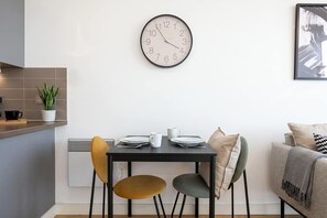 Une cuisine moderne avec une horloge murale ronde, une table à manger avec des chaises et un canapé dans l’espace salon.