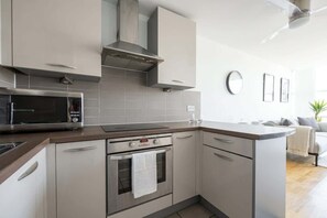 A modern kitchen with stainless steel appliances, a microwave, oven, and a built-in range hood. - Stunning Skyline 1BR Liverpool Apartment w Parking (Liverpool)