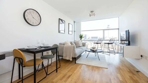 A modern living room with a dining area, a sofa, a coffee table, and a TV. - Stunning Skyline 1BR Liverpool Apartment w Parking (Liverpool)
