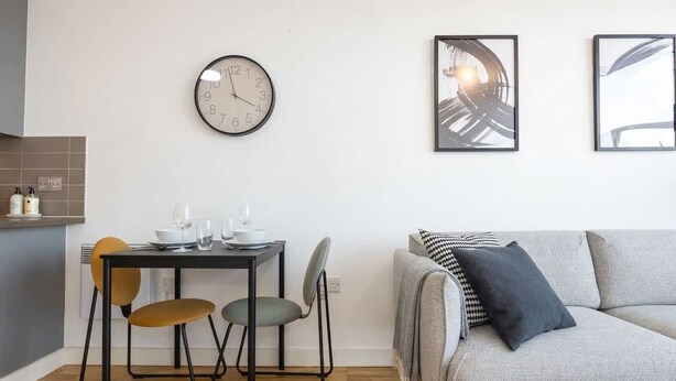Een moderne leefruimte met een eettafel, stoelen, een bank, een wandklok en abstracte kunst.