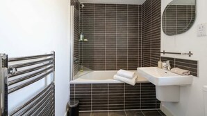 A bathroom with a bathtub, a sink, a mirror, and a shower. - Stunning Skyline 1BR Liverpool Apartment w Parking (Liverpool)