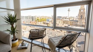 Een kamer met een groot raam met uitzicht op een stadsbeeld, met een potplant, twee stoelen en een bank.