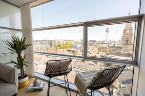 Una habitación con un ventanal grande con vistas a un paisaje urbano, que incluye una planta en maceta, dos sillas y un sofá.