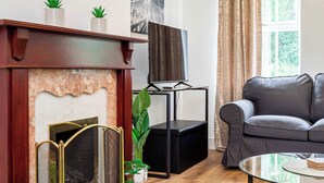 A living room with a fireplace, a grey sofa, a TV on a stand, and a green rug.
